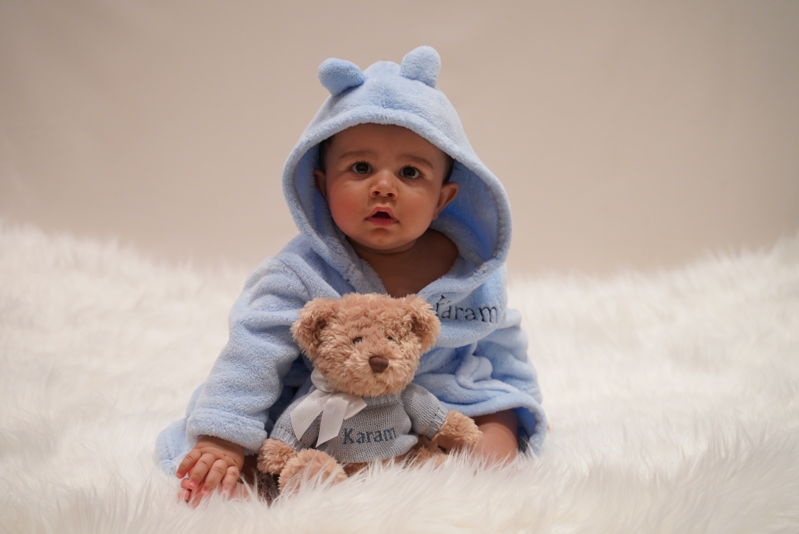 Baby wearing a blue hood and holding a teddy bear in the studio