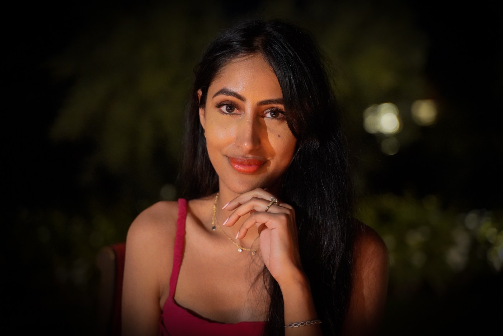 A woman in a pink top photographed in warm light against a softly blurred dark background
