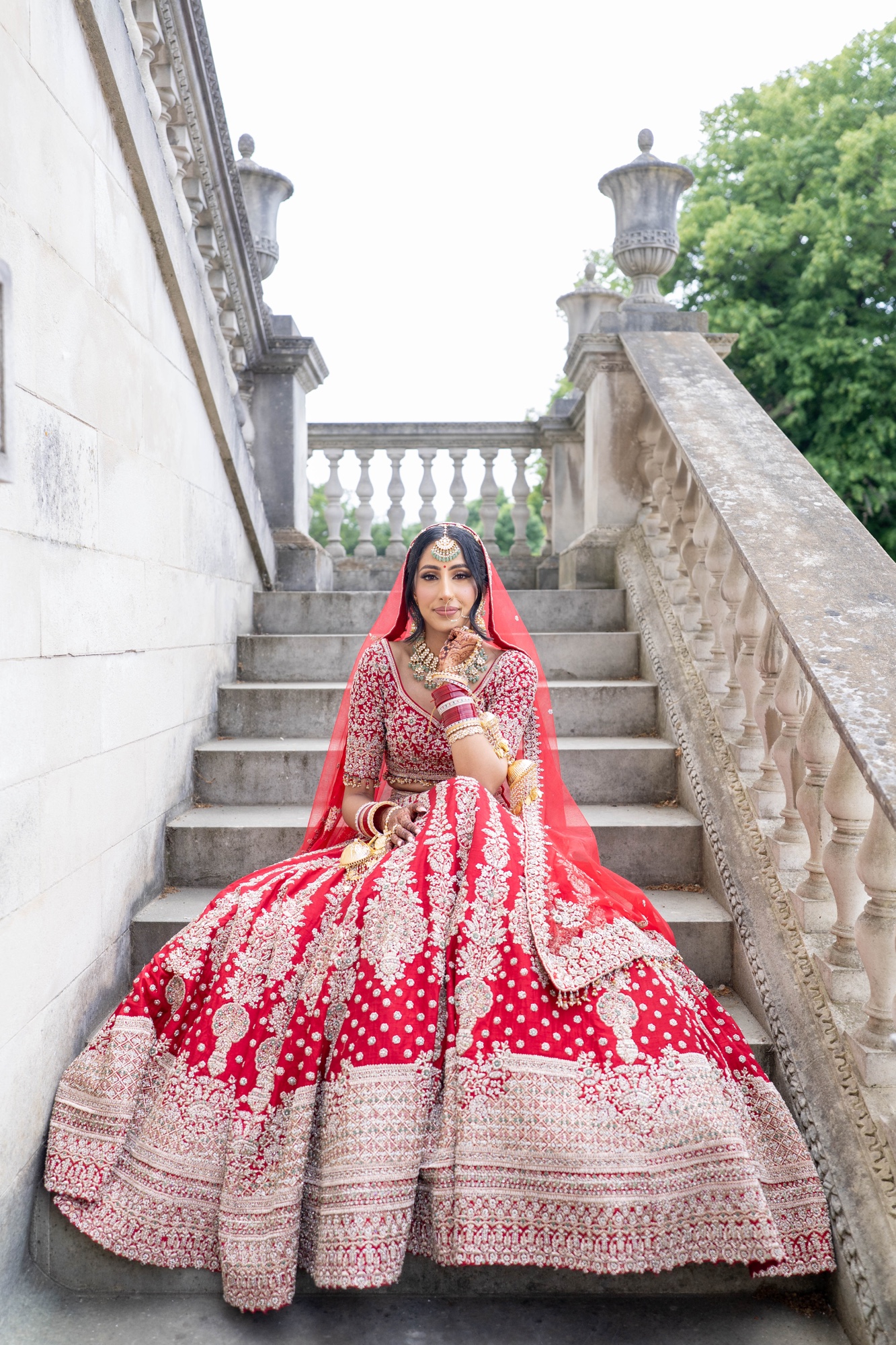 Bride seated on a stone staircase in her detailed red wedding dress