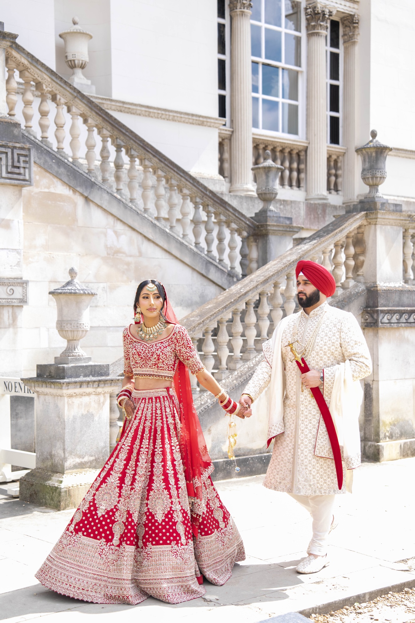 Sikh bride and groom walking together beside a grand staircase